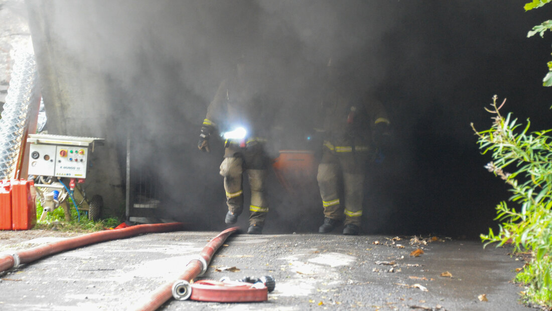 Two firefighters emerge from a tunnel with heavy smoke during a fire trial in the Piottino Tunnel