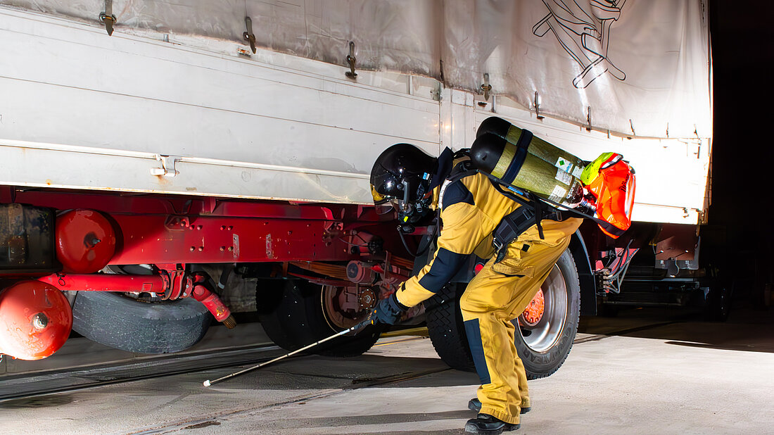 Ein Feuerwehrmann sucht die Fläche unter einem LKW mit dem Suchstock ab.