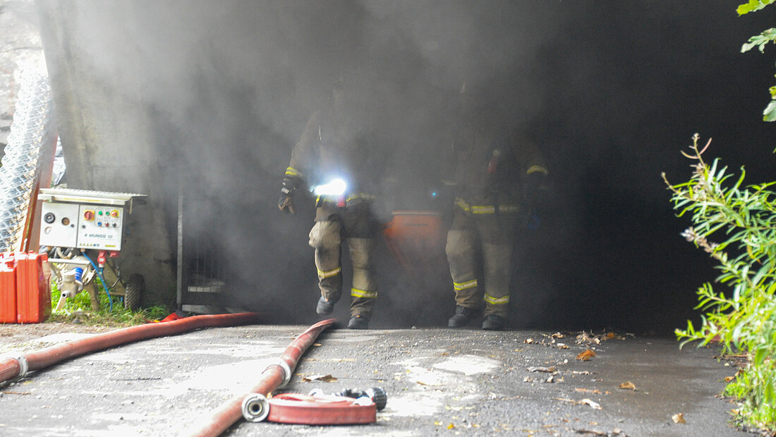 Essais avec feu réel menés dans le tunnel du Piottino. Deux pompiers sortent d'un tube de tunnel très enfumé lors d'un essai d'incendie dans le tunnel de Piottino