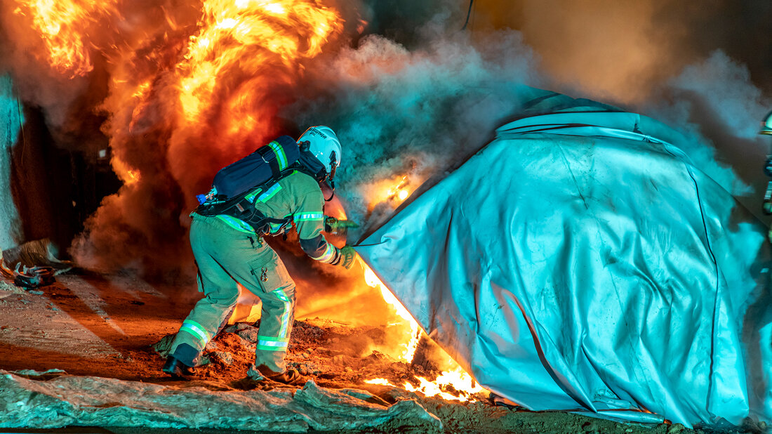 Feuerwehrangehörige ziehen eine Löschdecke über ein brennendes Elektro-Fahrzeug.