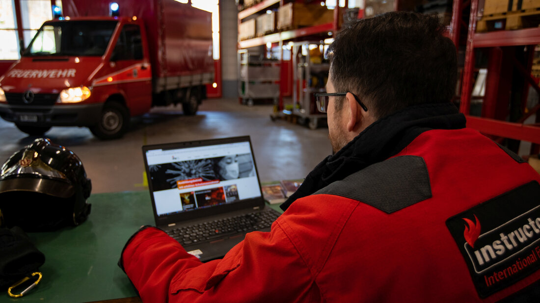 A firefighter at a laptop with the International Fire Academy website opened up