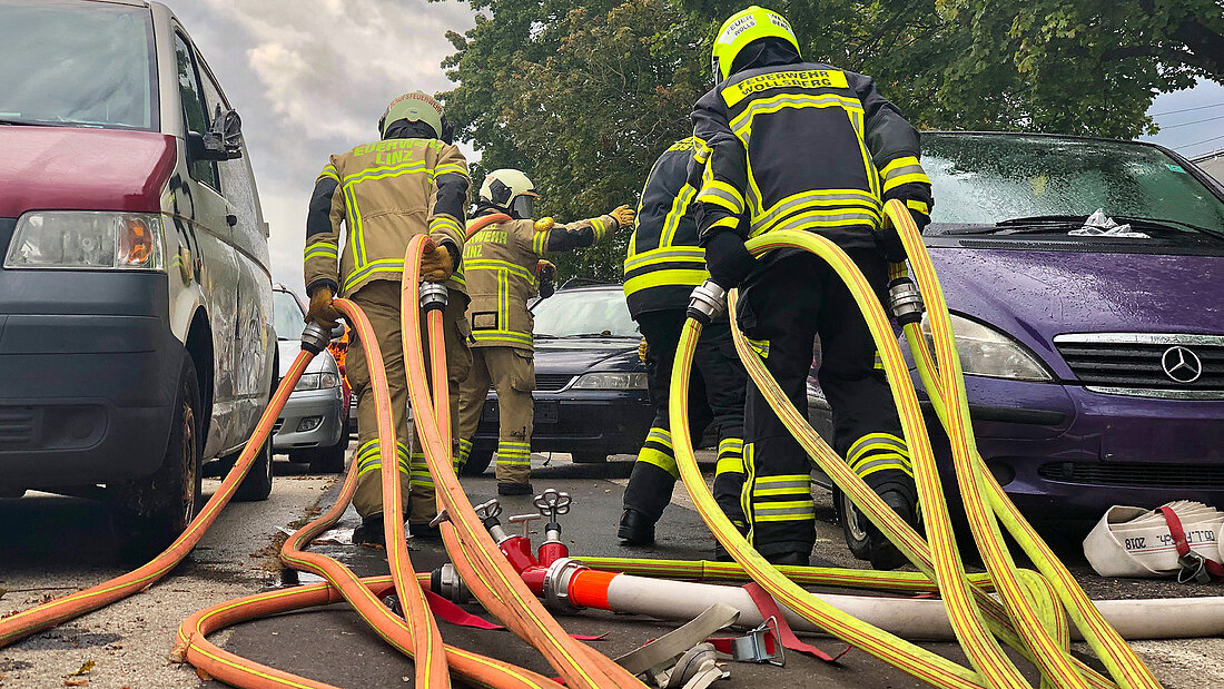 Feuerwehrangehörige ziehen Schläuche zwischen Fahrzeugen
