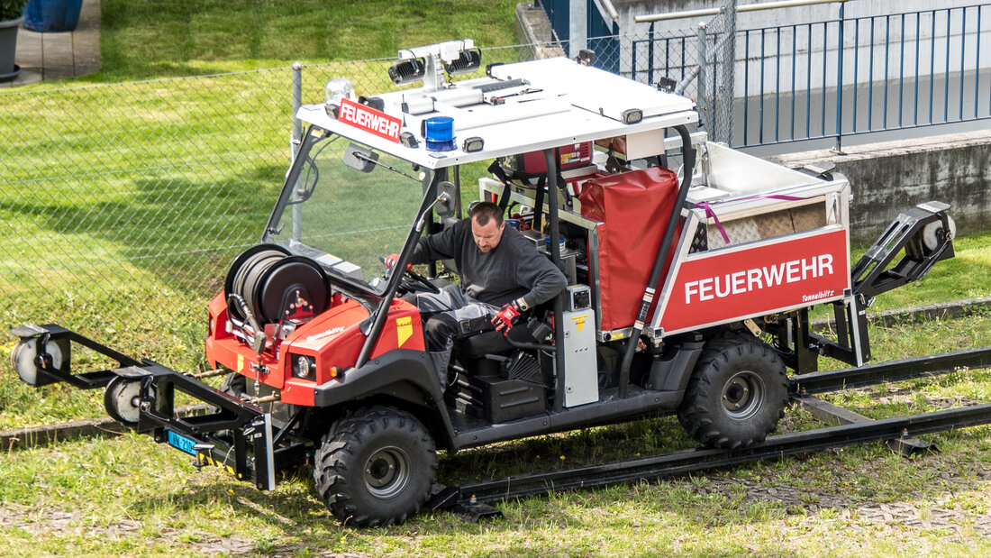 Zweiwegefahrzeug einer Feuerwehr, das auf Strassen und Schienen fahren kann, wobei die Gummiräder auf den Schienen laufen und ein Spurführungsmechanismus das Fahrzeug lenkt.