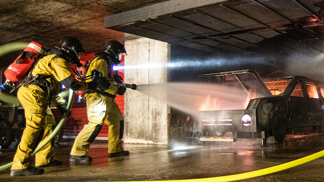 Deux sapeurs-pompiers s’entraînent à éteindre un véhicule dans un parking souterrain.