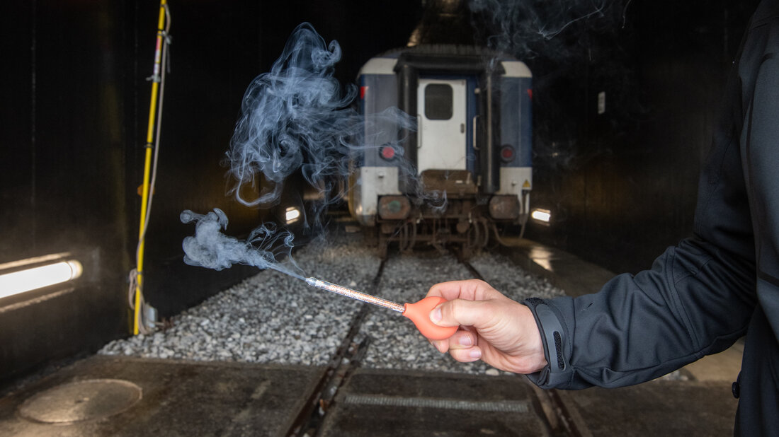 Smoke rises from a tube and indicates the direction of airflow in front of a portal of a railway tunnel.