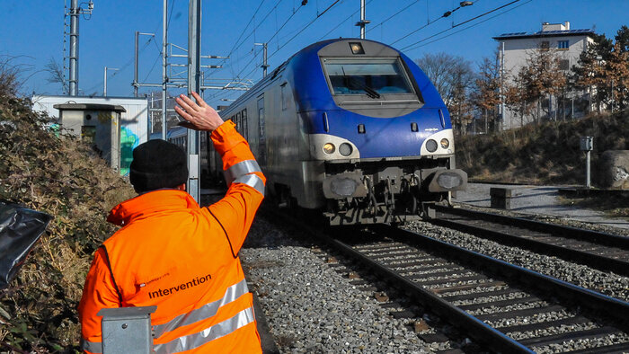 Person im Gleisbereich kommuniziert per Handzeichen mit einem Lokführer